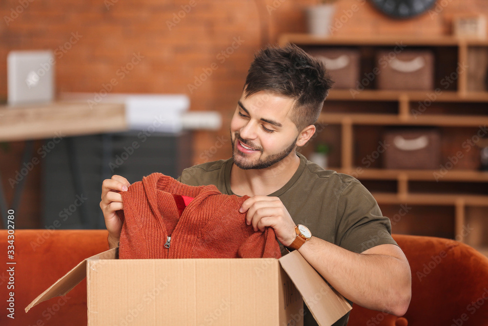 Young man unpacking box with new clothes at home