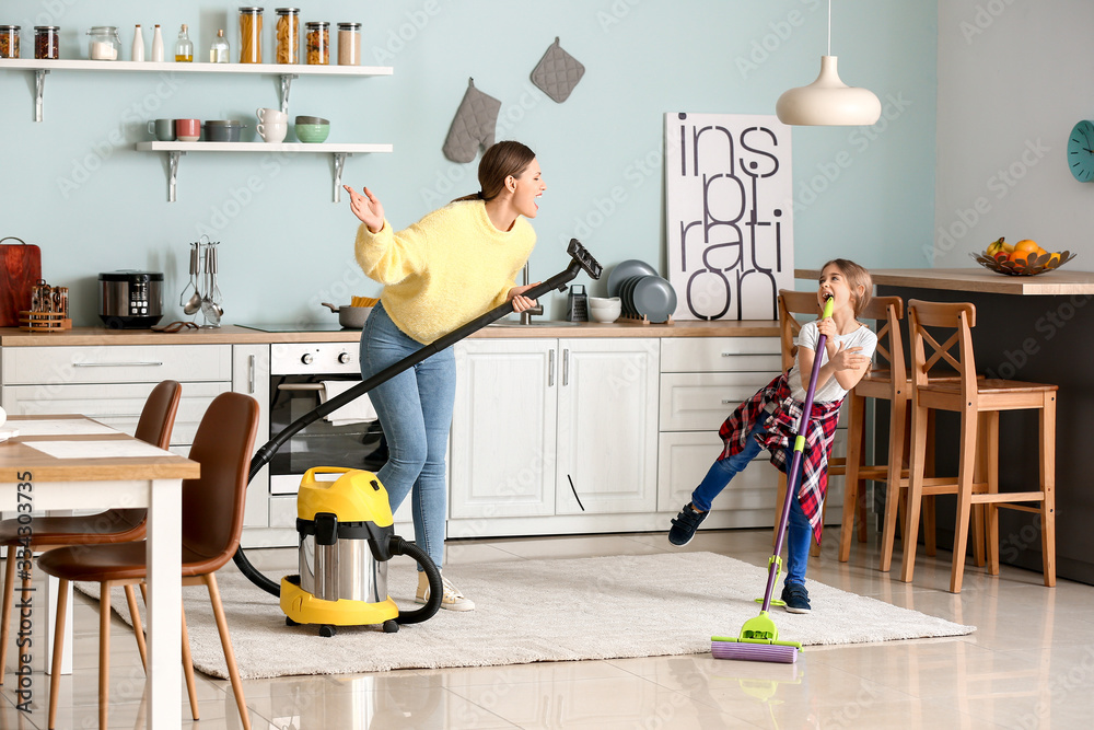 Young woman with her little daughter having fun while cleaning kitchen