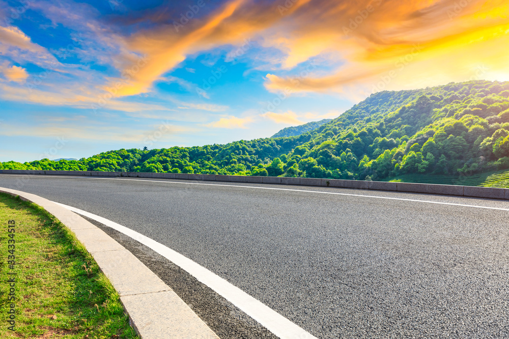 Empty asphalt road and green tea plantation nature landscape at sunset.