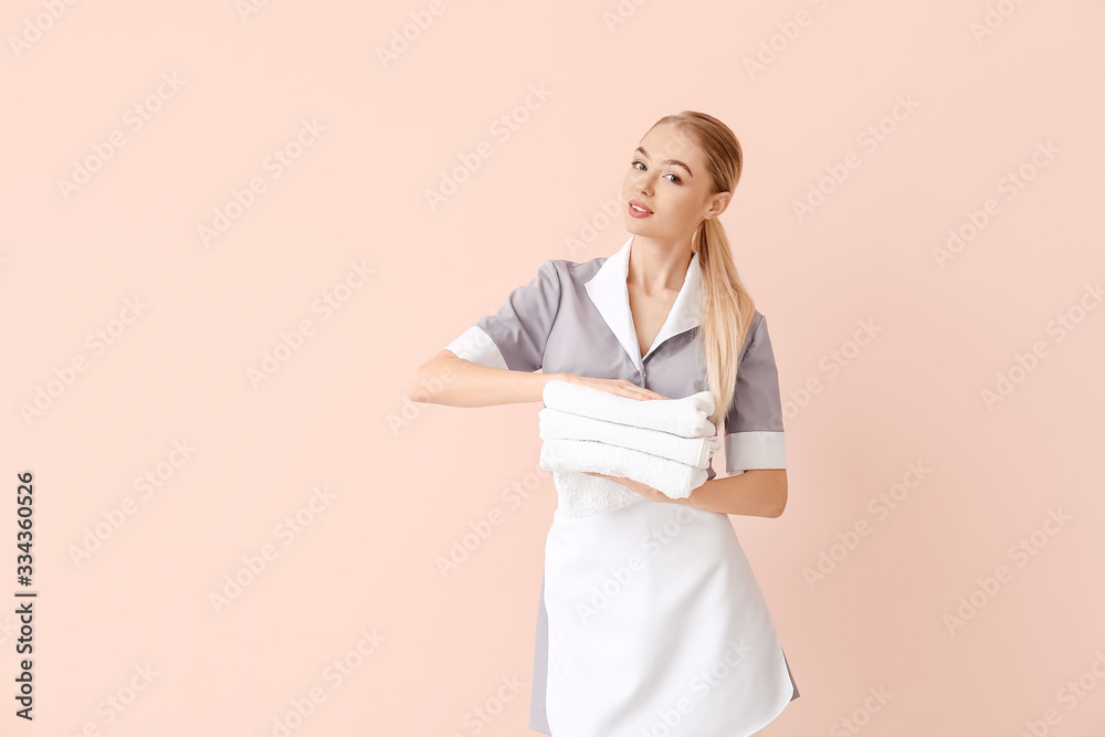 Beautiful young chambermaid with towels on color background