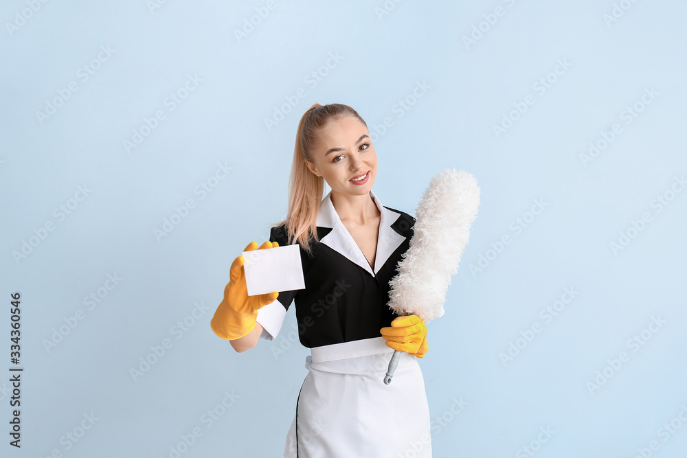 Beautiful young chambermaid with business card on color background