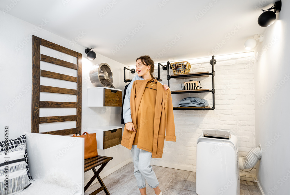 Young woman trying a jacket, choosing clothes to wear in the modern small wardrobe at home