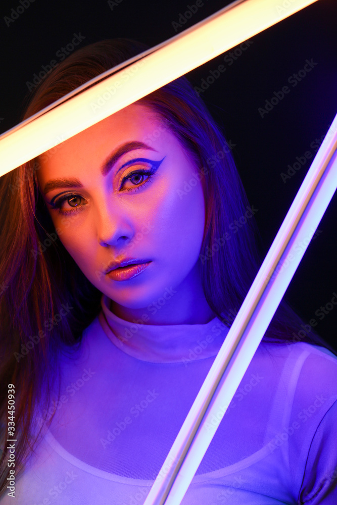 Toned portrait of beautiful woman with neon lamps on dark background