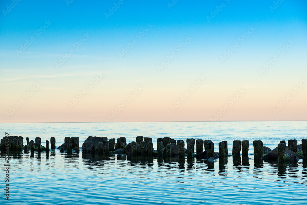 Big stones on the beach, and damaged wooden breakwater.  Sea coast of  island of Rugen. Dusk.