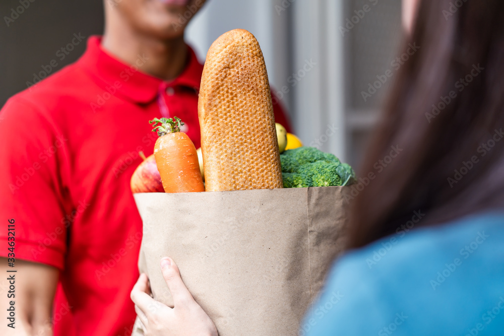 Asian deliver man worker in red color uniform handling bag of food, fruit, vegetable give to young b