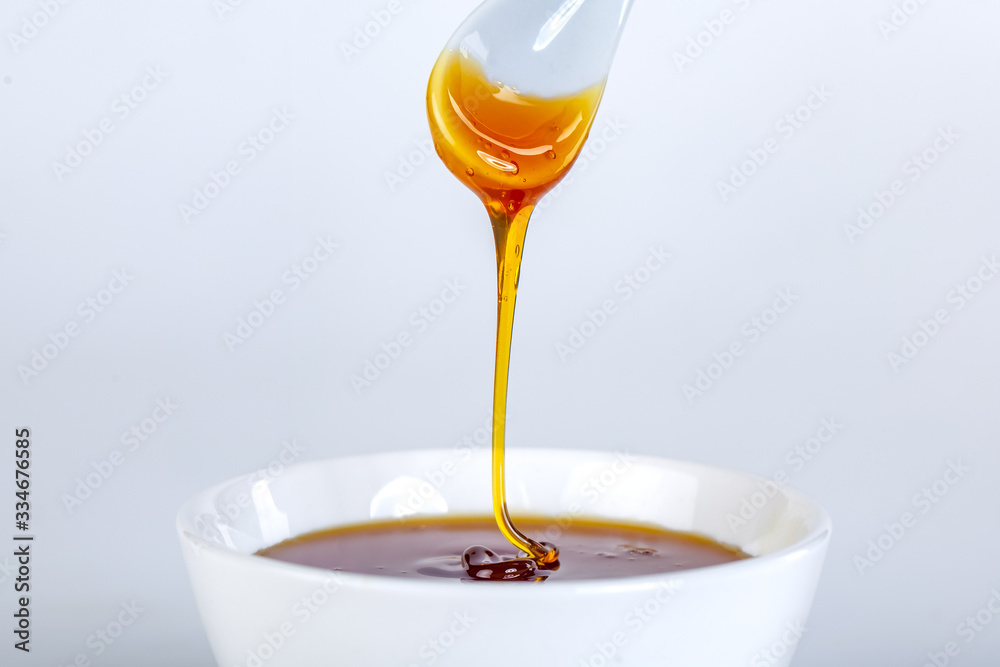 honey dripping from ceramic spoon to ceramic bowl