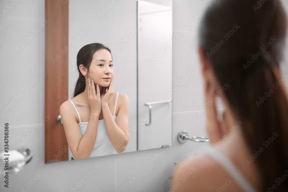 Beauty in mirror reflection. Over the shoulder view of beautiful woman touching her face while looki