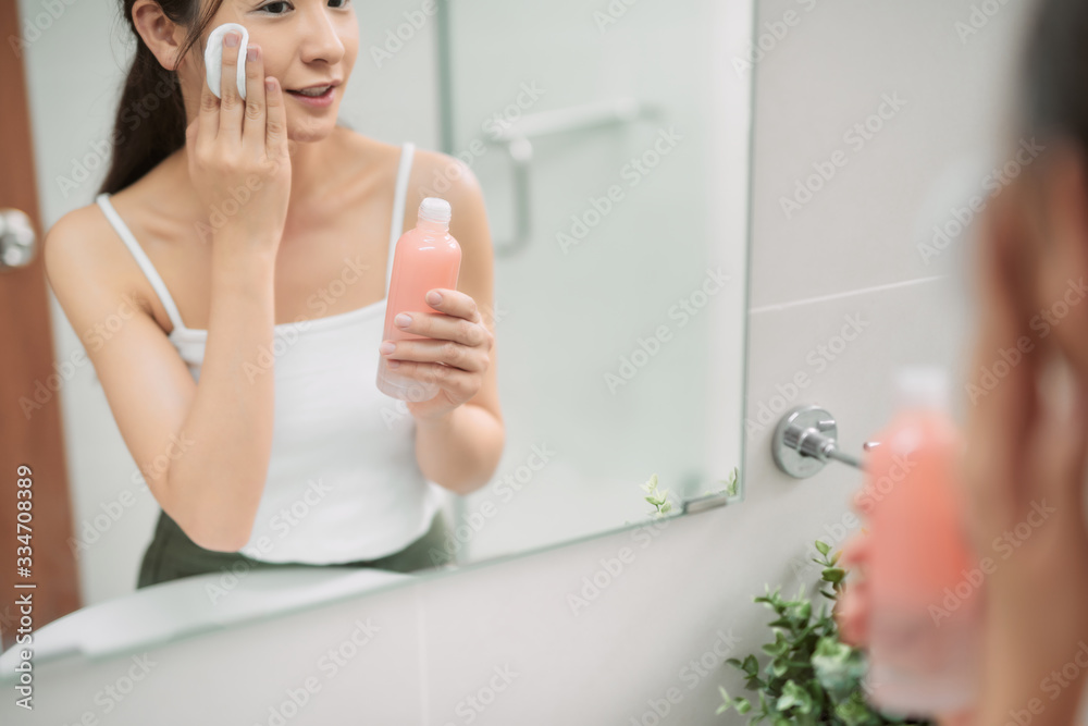 Young attractive woman looking at mirror, cleanses the face with a cotton pad after a shower at the 