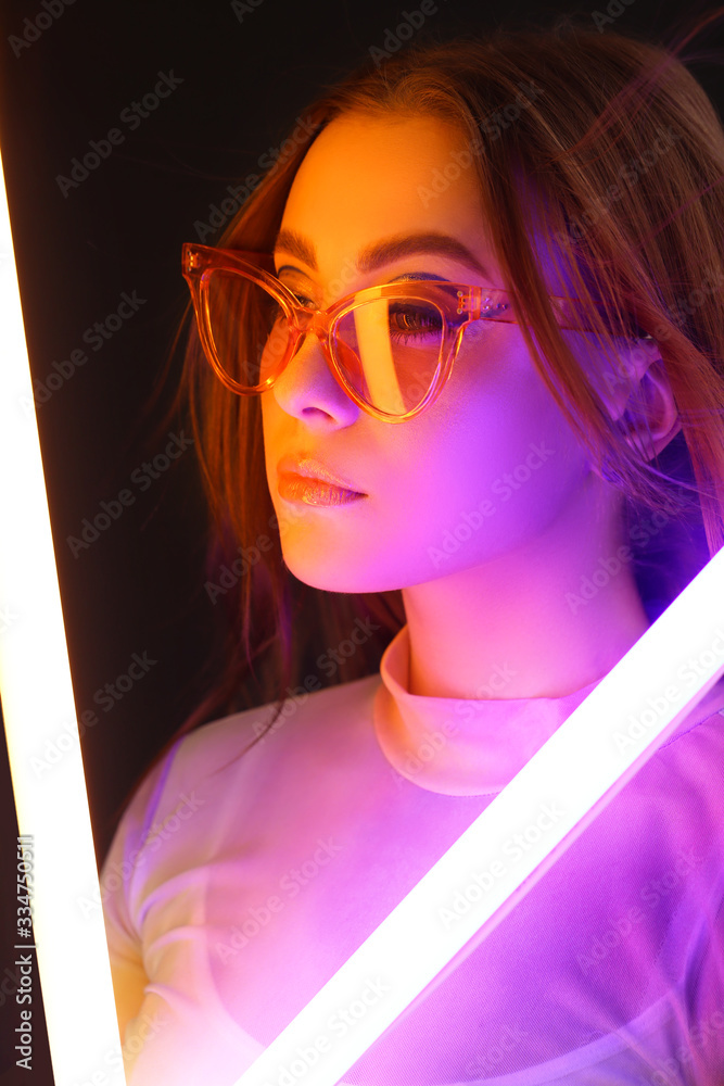 Toned portrait of beautiful woman with neon lamps on dark background