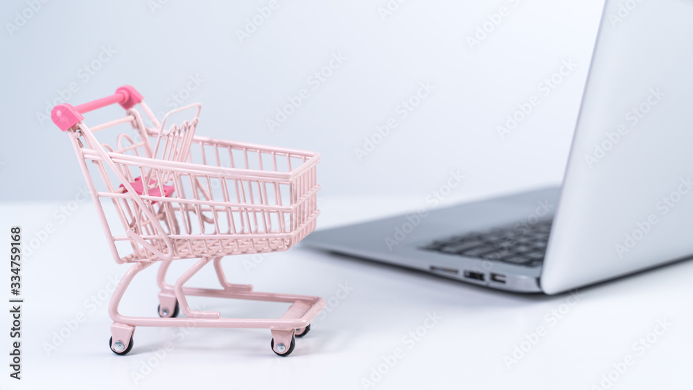 Online shopping. Mini empty pink shop cart trolley over a laptop computer on white table background,