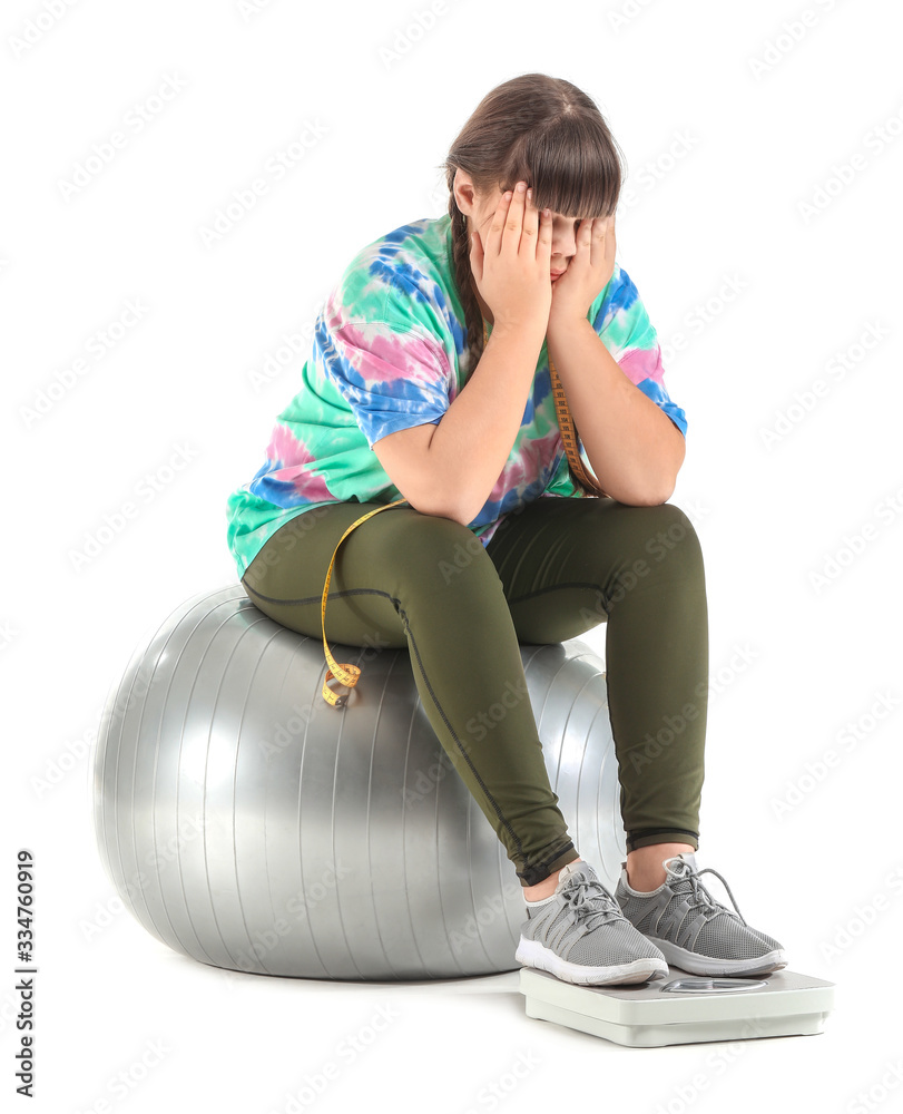 Sad overweight girl with measuring scales and fitness ball on white background