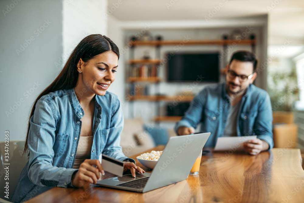 Portrait of a beautiful smiling woman paying bills online. Couple at home. People, technology and fi