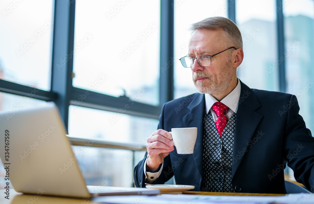 Businessman wears neat suit. Male with cup of coffee at table with laptop on it. Coffee brake at wor