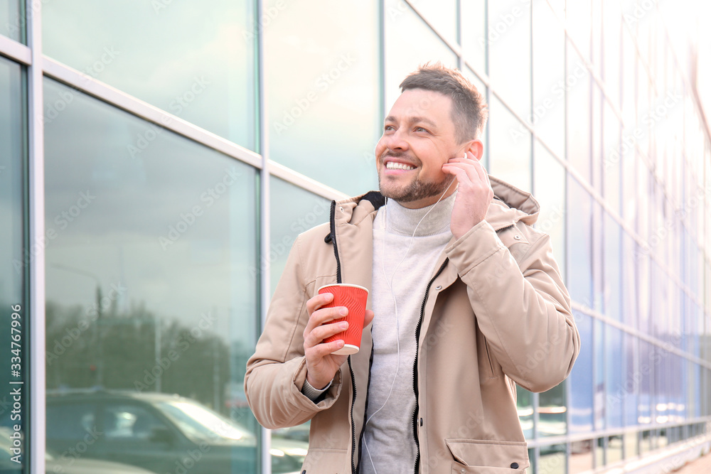 Handsome man with cup of coffee listening to music outdoors