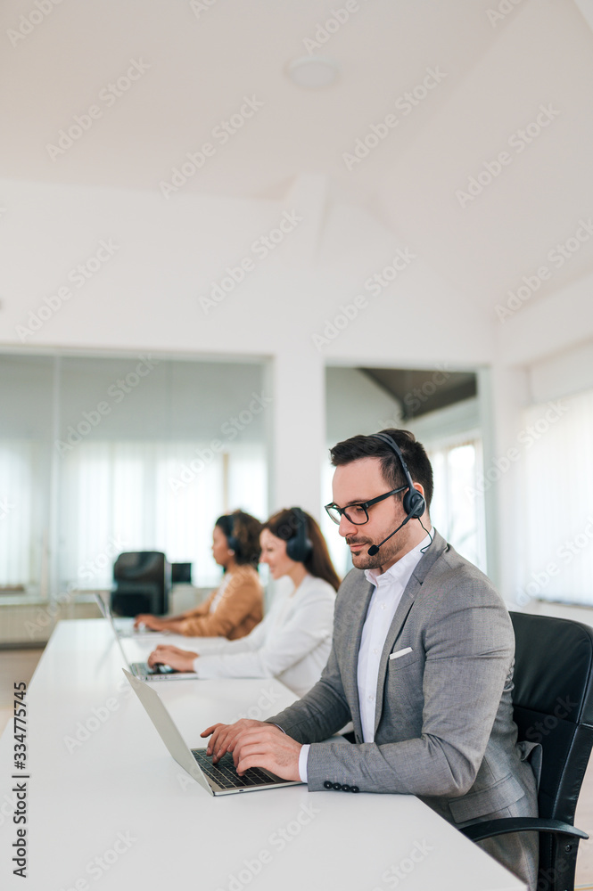 Businessman wearing headset working on a laptop, portrait,