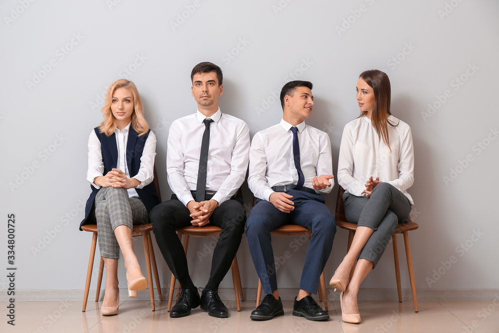 Young business people waiting in line near light wall