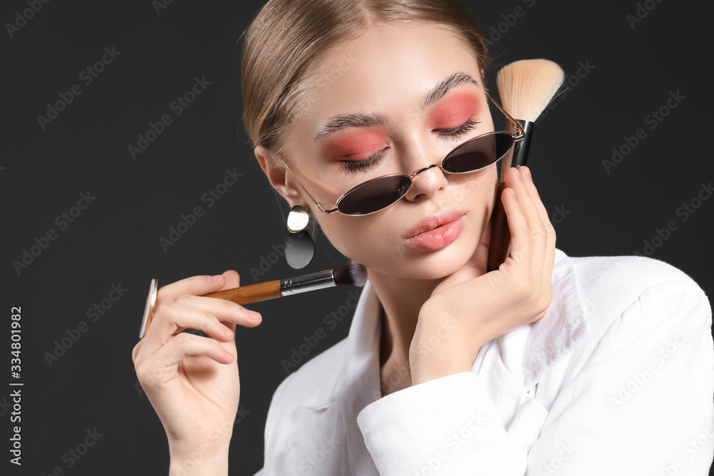 Beautiful fashionable woman with makeup brushes on dark background