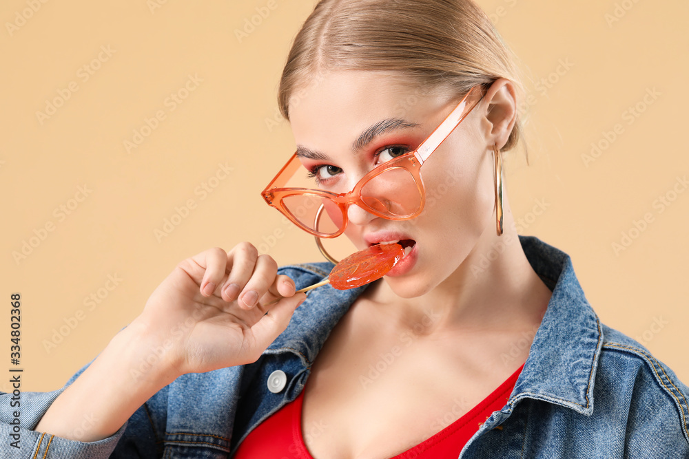 Beautiful fashionable woman with lollipop on color background