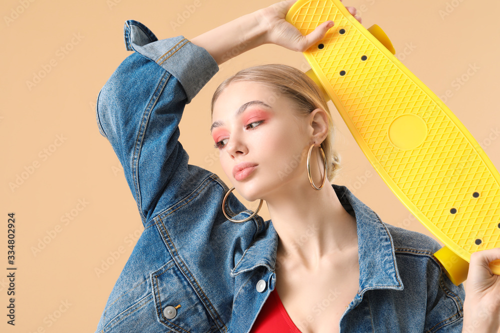 Beautiful fashionable woman with skateboard on color background