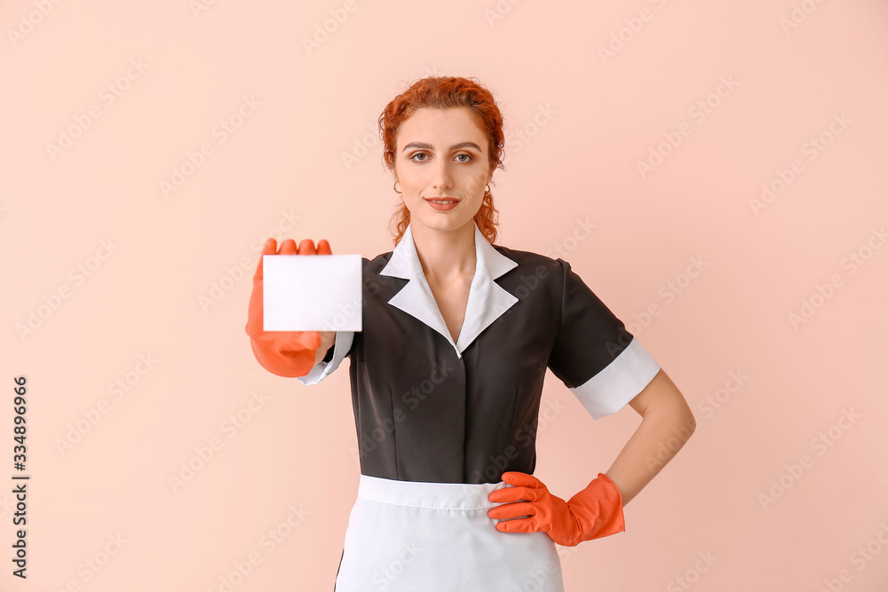 Beautiful young chambermaid with business card on color background