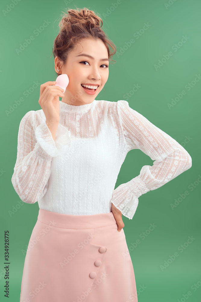 Asian woman laughing and holding facial sponge isolated over green background