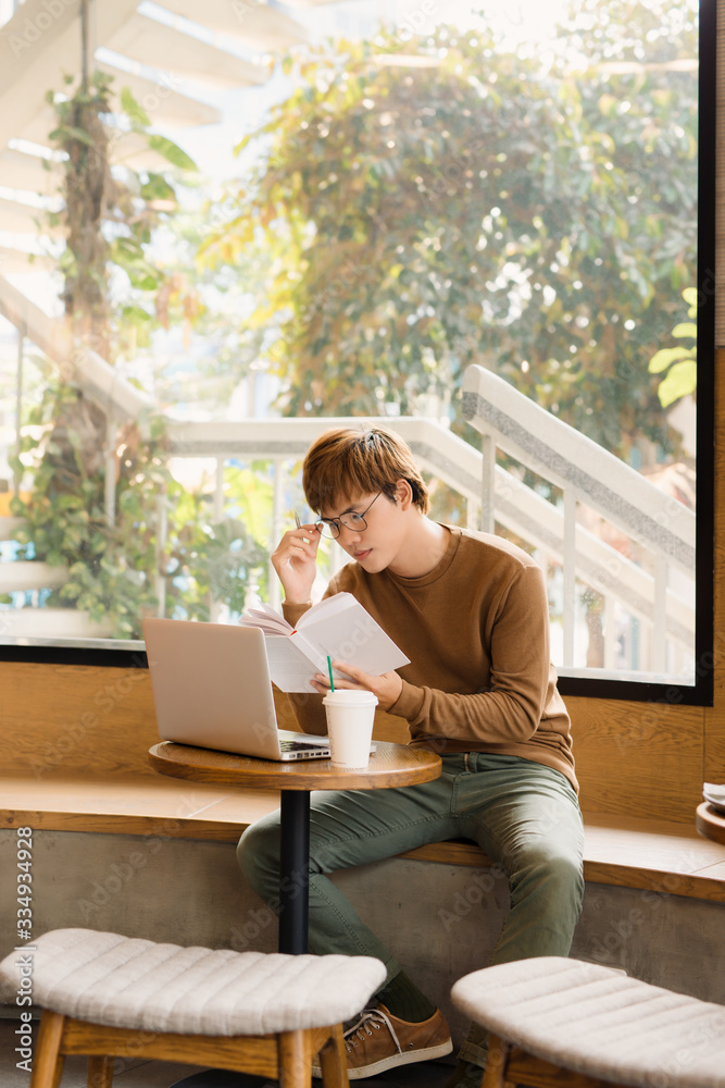 Businessman using laptop with tablet and pen on wooden table in coffee shop with a cup of coffee