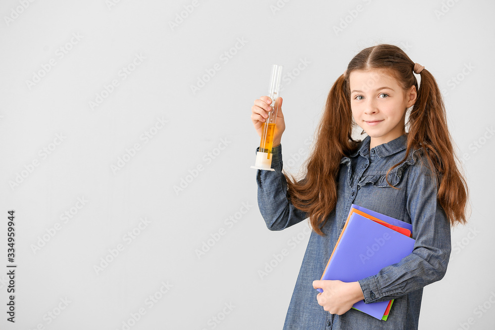 Cute little schoolgirl with laboratory glassware on grey background