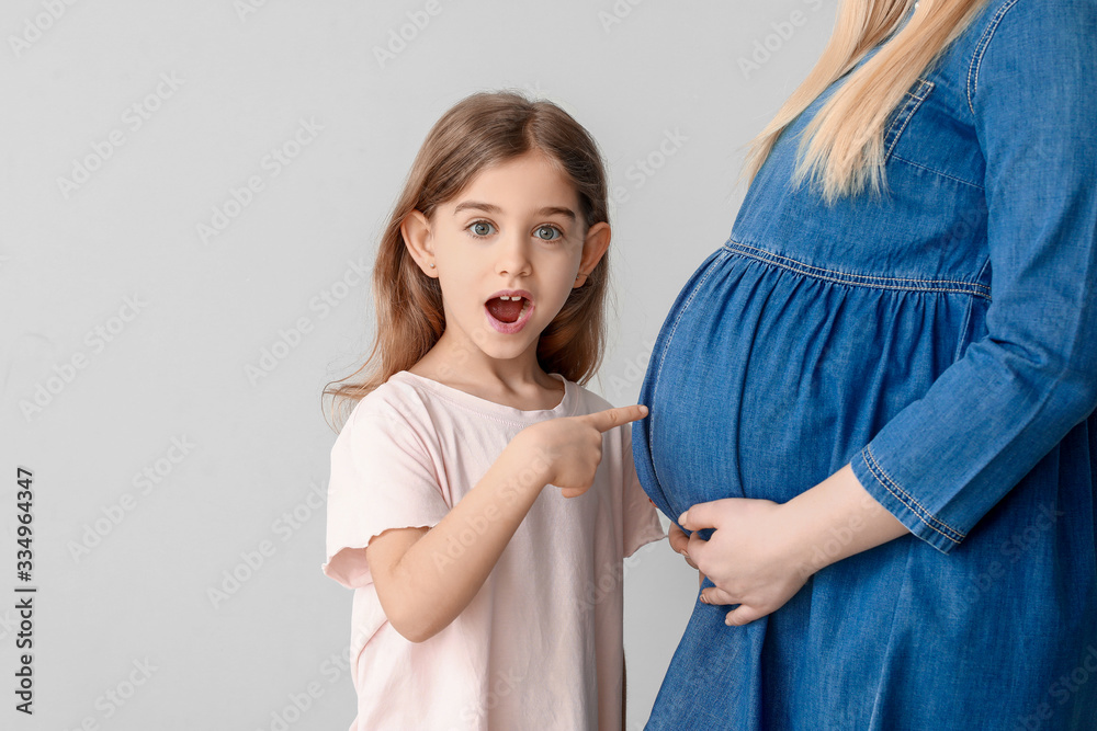 Beautiful pregnant woman and her surprised little daughter against light background