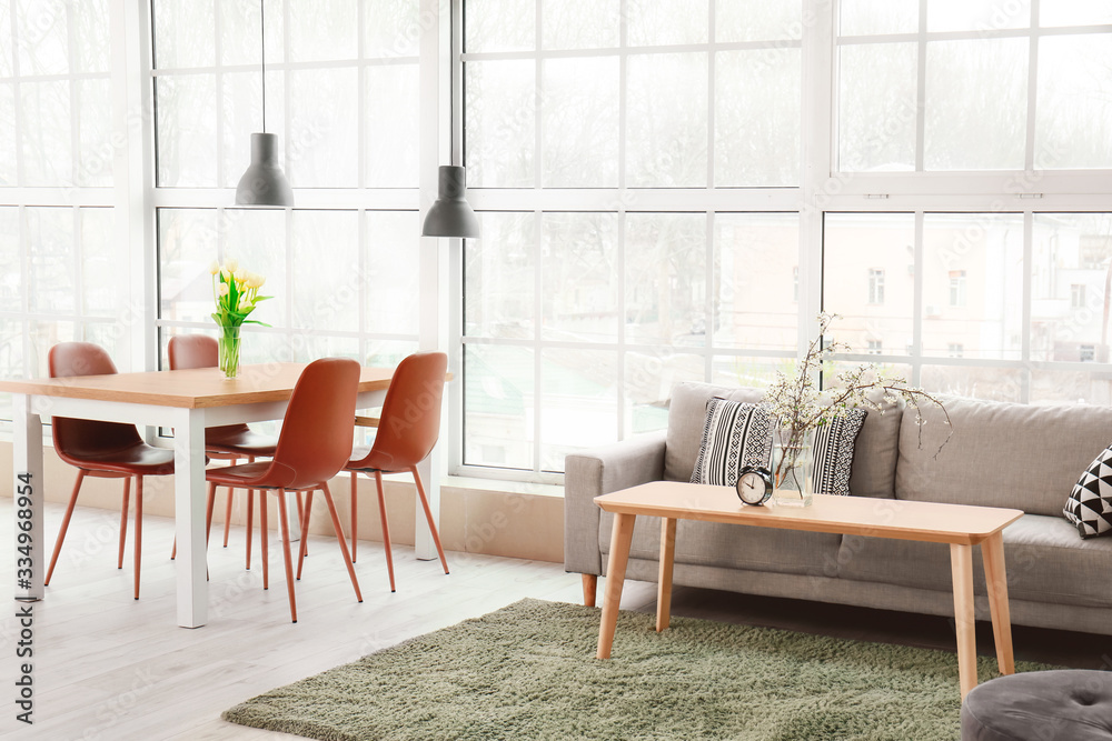 Interior of modern room with comfortable sofa, tables and spring flowers