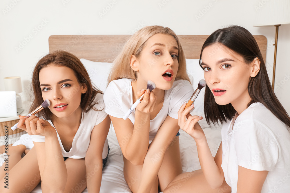 Beautiful young women applying makeup in bedroom