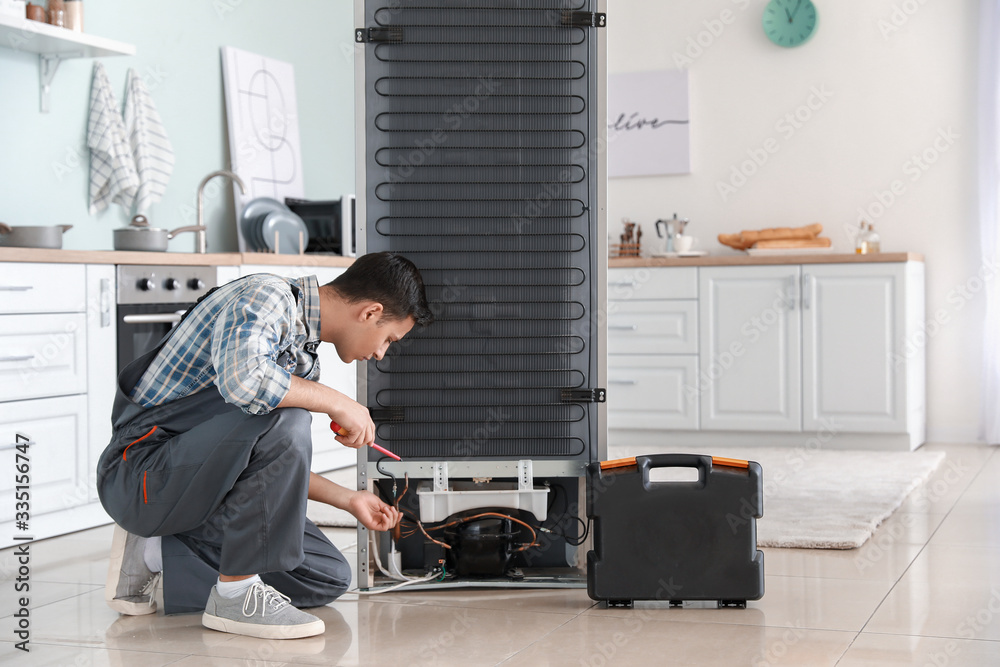 Worker repairing refrigerator in kitchen