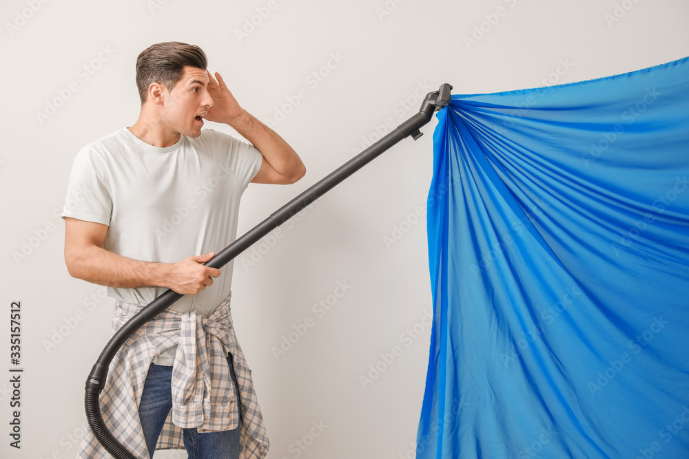 Afraid young man with sucked into vacuum cleaner curtain against white background