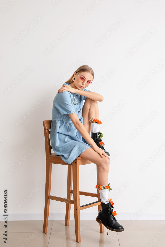 Beautiful fashionable woman sitting on chair near light wall