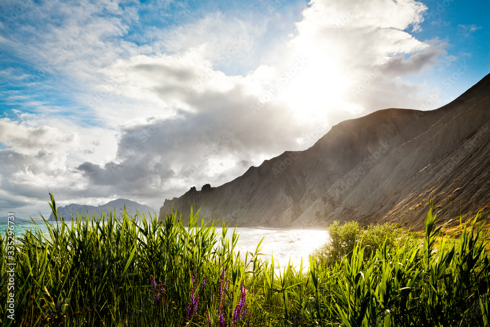 Grass, sea and mountains at background. Cloudy sky