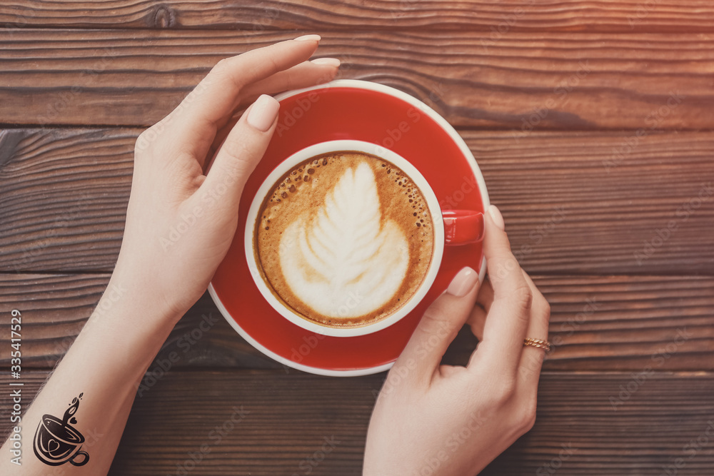 Woman drinking tasty cappuccino at wooden table