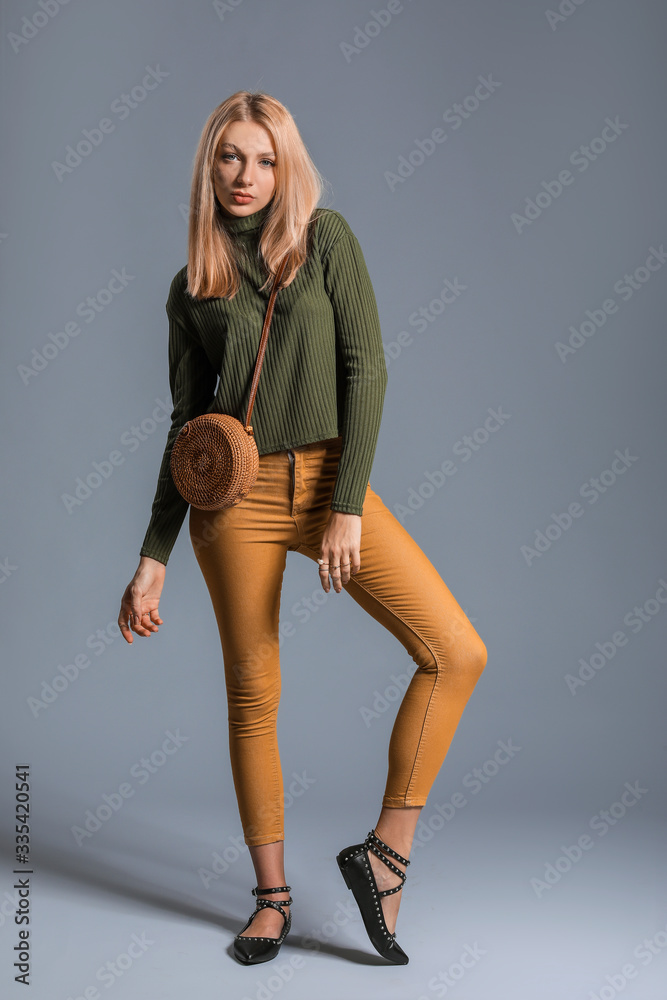 Young woman in warm sweater and with stylish bag on grey background