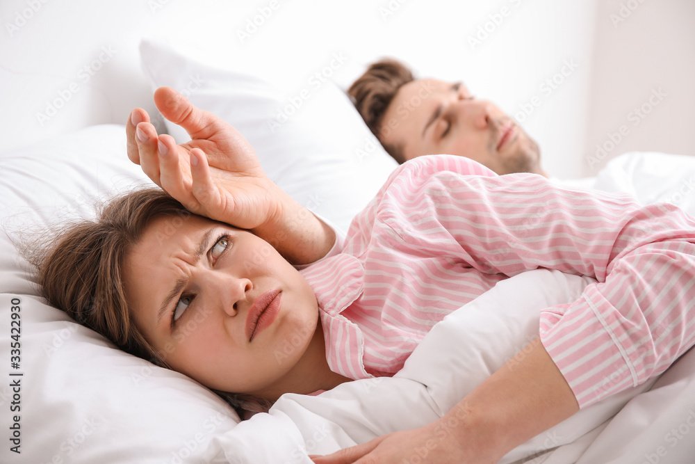 Young woman feeling discomfort while sleeping in bed with her husband