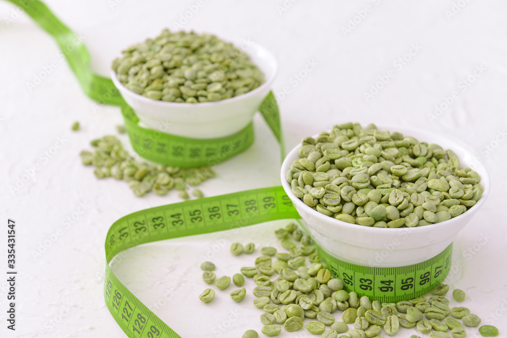 Bowls with green coffee beans and measuring tape on white background