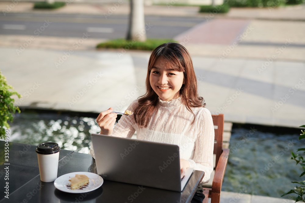 Beautiful woman eating delicious banana cake in a coffee shop. Girl in front of laptop in a coffee s