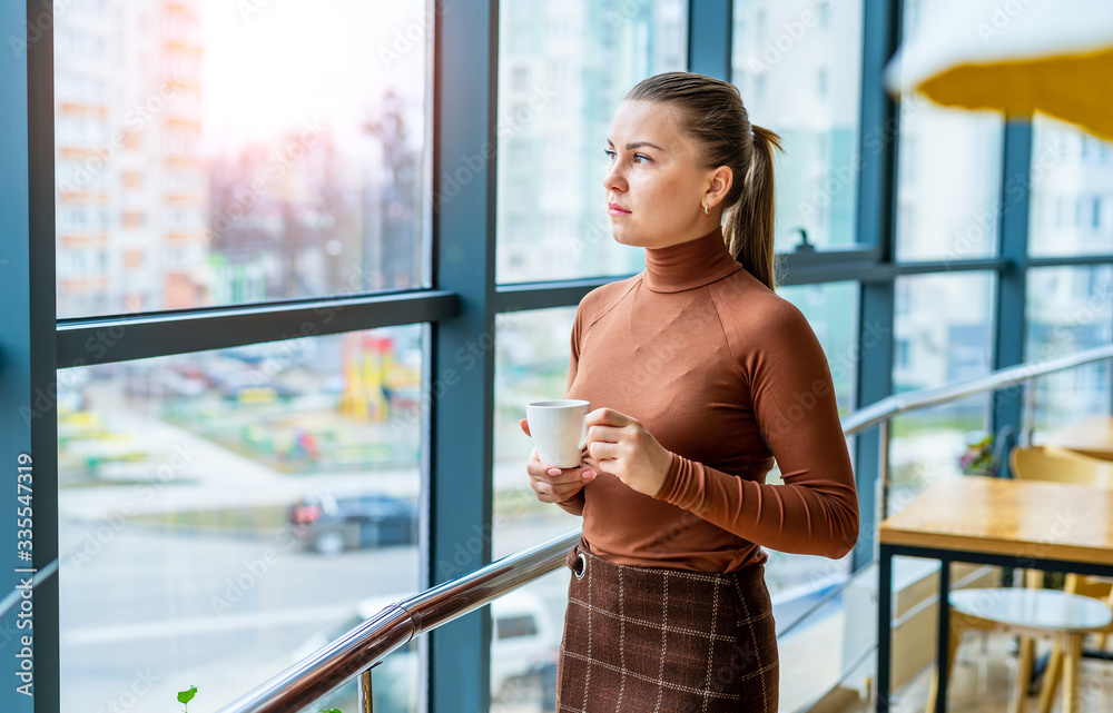 Pretty office employee drinking coffee isolated near window. Panoramic city view.