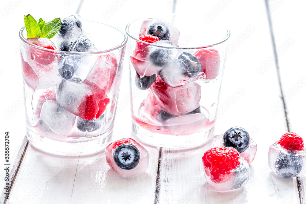 Icecubes with blueberry and raspberry in glass on wooden table