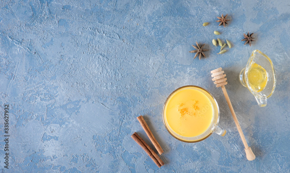 Cup of golden turmeric latte milk with curcuma powder on gray. Top view.