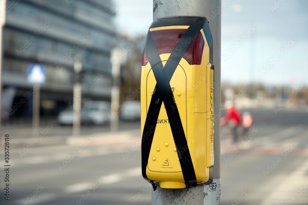 Yellow pedestrian crossing sign or pedestrian crossing button located on a metal pillar next to a pe