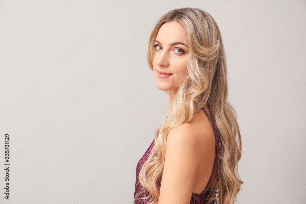 Beautiful young woman with curly hair on light background