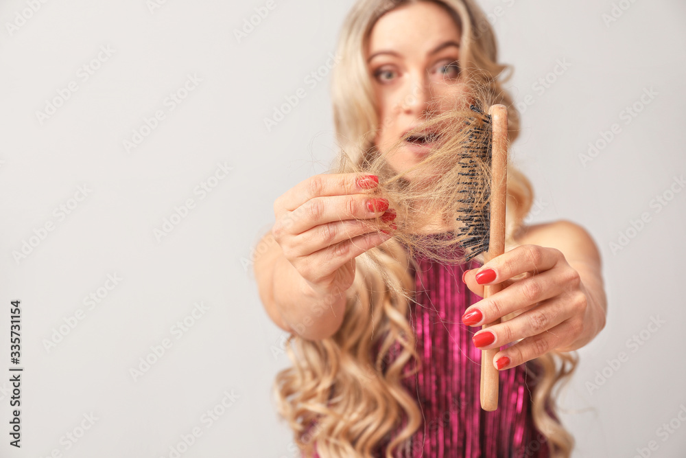 Worried woman with hair loss problem on light background