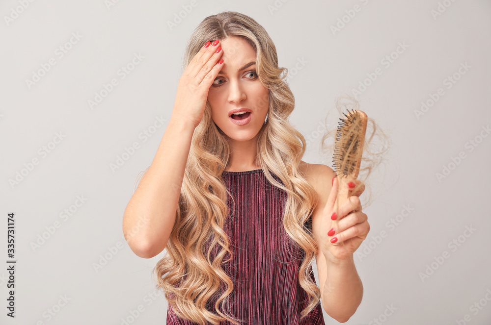 Worried woman with hair loss problem on light background