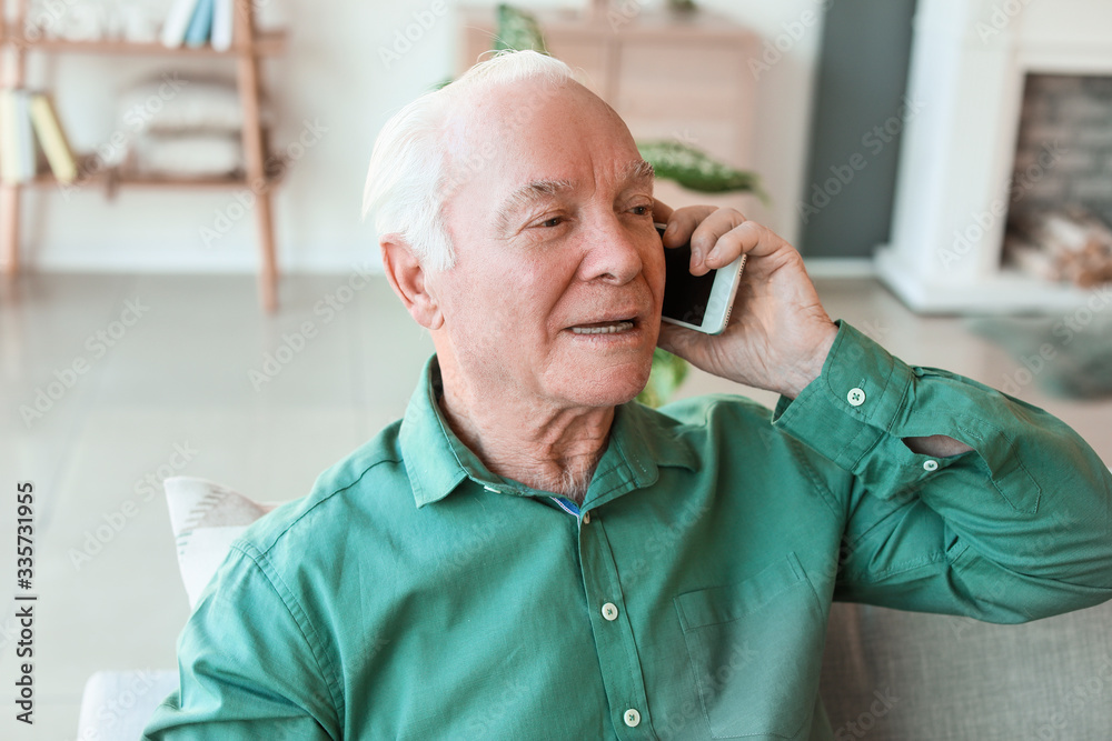 Elderly man talking by mobile phone at home