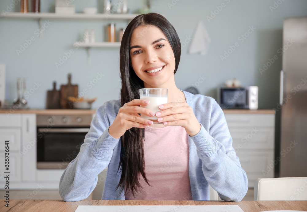 Beautiful young woman drinking milk in kitchen