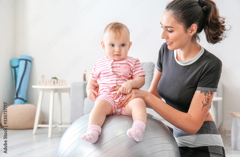 Young sporty mother and her baby doing exercises with fitball at home