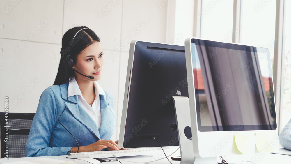 Customer support agent or call center with headset works on desktop computer while supporting the cu